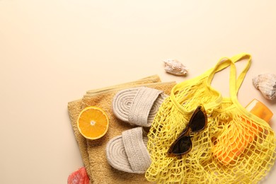 Photo of String bag, different beach accessories and orange on beige background, top view. Space for text