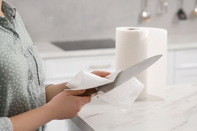 Photo of Woman wiping knife with paper towel at white marble table in kitchen, closeup