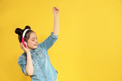 Cute girl enjoying music in headphones on color background. Space for text