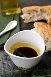 Photo of Bowl of organic balsamic vinegar with oil, thyme and bread on table, closeup