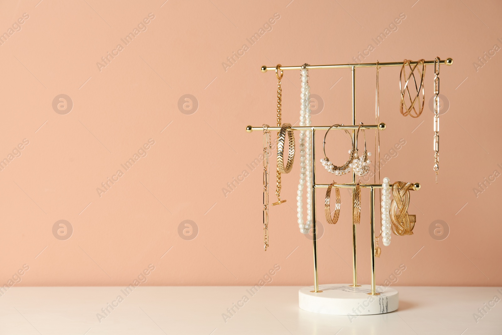 Photo of Holder with set of luxurious jewelry on white table near pale pink wall, space for text