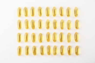 Yellow vitamin capsules on white background, flat lay