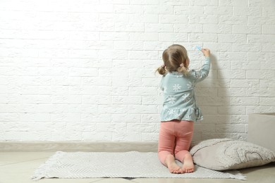 Little girl drawing on white brick wall indoors, back view and space for text. Child`s art