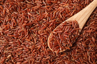 Wooden spoon with cereal on raw brown rice, top view. Space for text