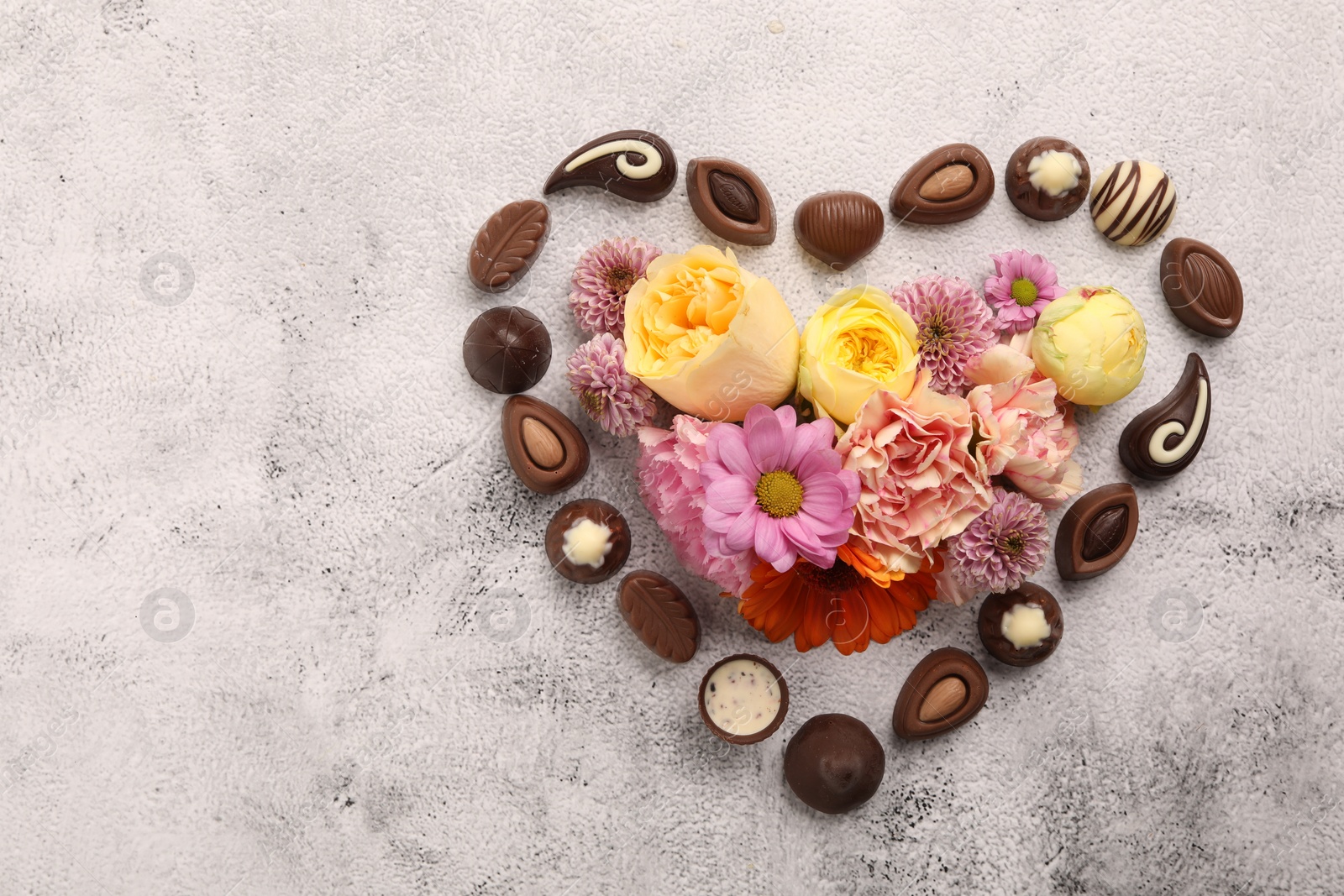 Photo of Heart made with delicious chocolate candies and beautiful flowers on grey table, flat lay. Space for text