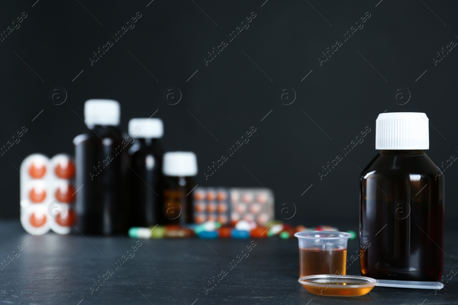 Photo of Bottle of cough syrup, dosing spoon and measuring cup on black table. Space for text