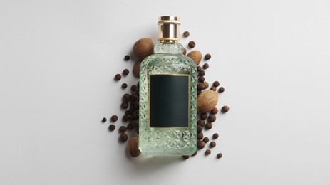 Bottle of perfume surrounded by allspice and nutmegs on white background, top view