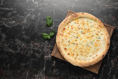 Photo of Delicious cheese pizza and basil on black marble table, flat lay. Space for text