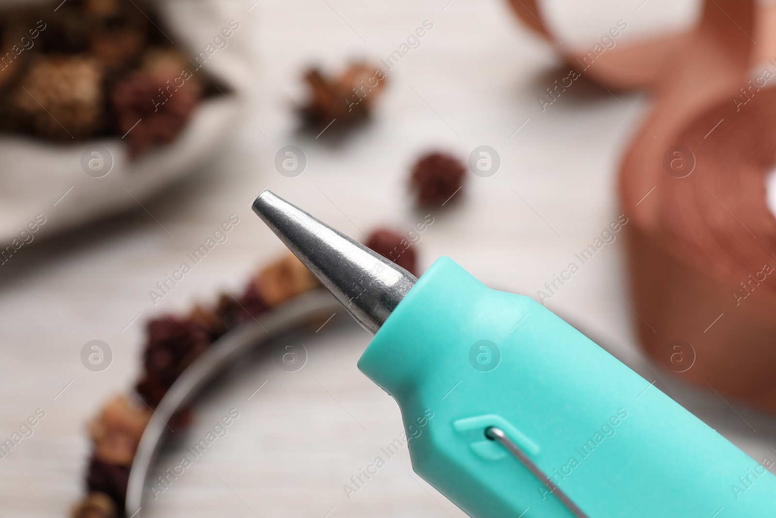 Photo of Hot glue gun over table with handicraft materials, closeup