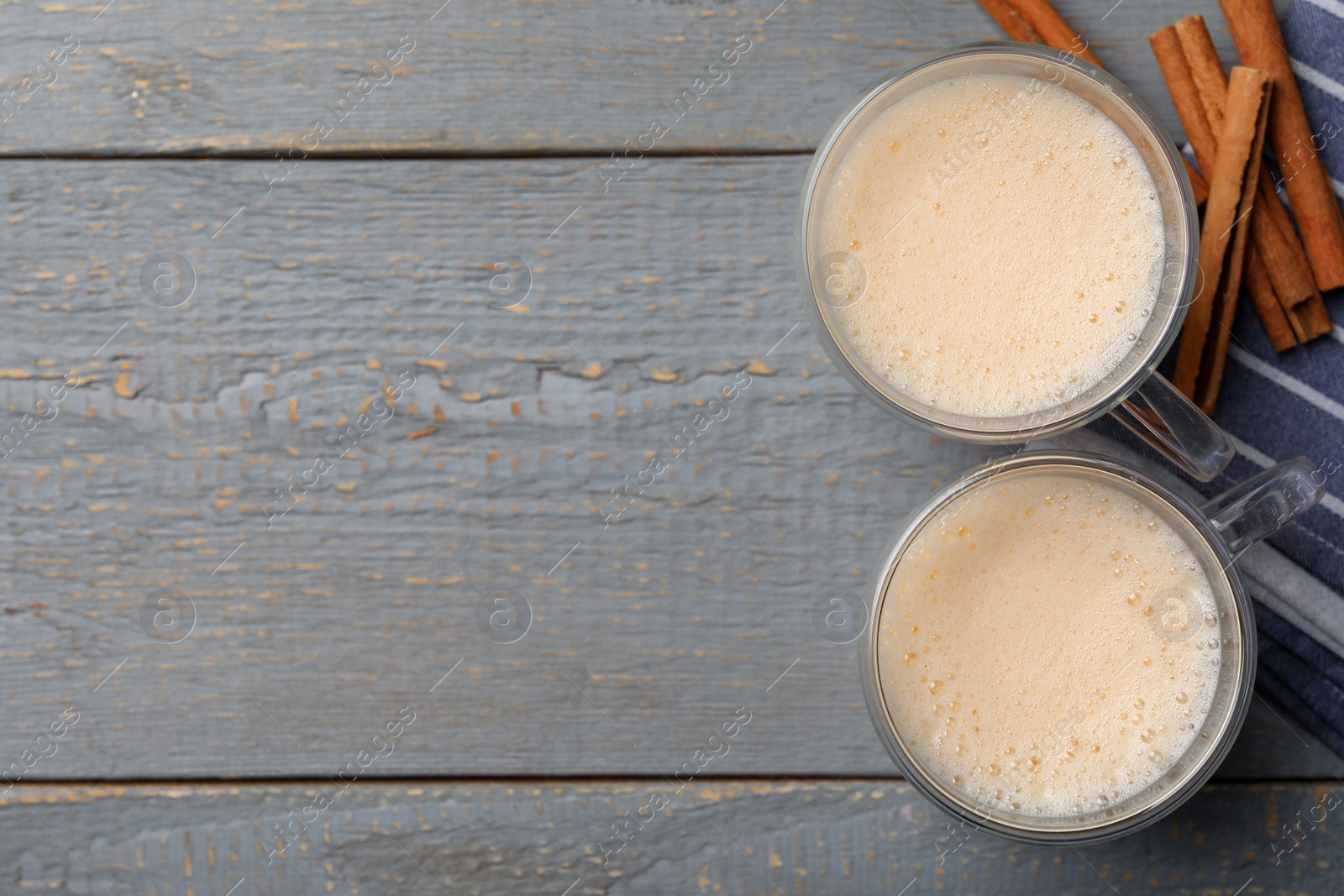 Photo of Delicious eggnog with cinnamon on grey wooden table, flat lay. Space for text