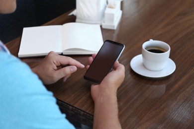 Man with smartphone at table in cafe, closeup