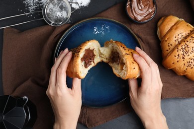 Photo of Woman eating tasty croissant with chocolate at table, top view