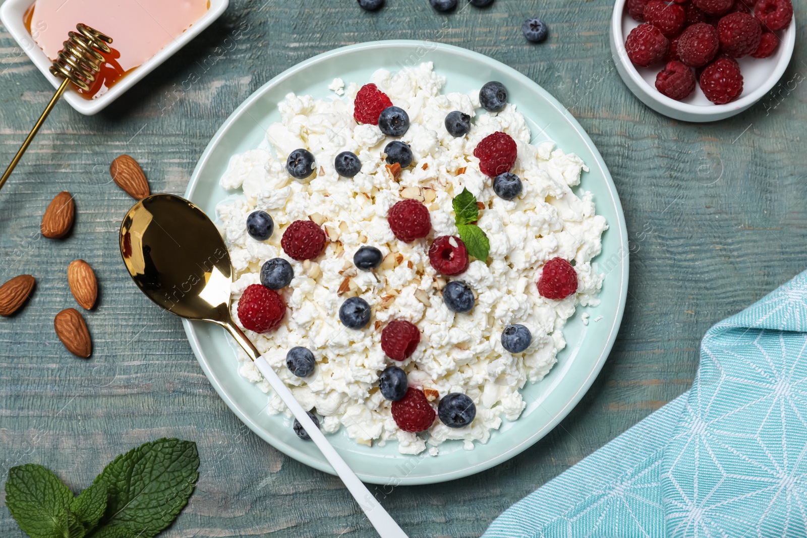 Photo of Delicious cottage cheese with fresh berries and honey served for breakfast on light blue wooden table, flat lay