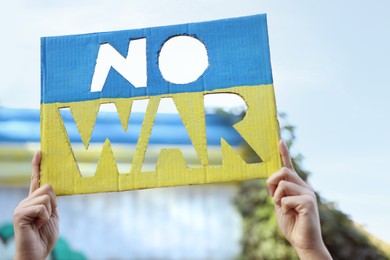 Photo of Woman holding poster in colors of Ukrainian flag with words No War outdoors, closeup