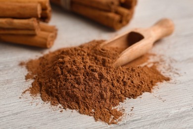 Aromatic cinnamon powder and sticks on white wooden table, closeup