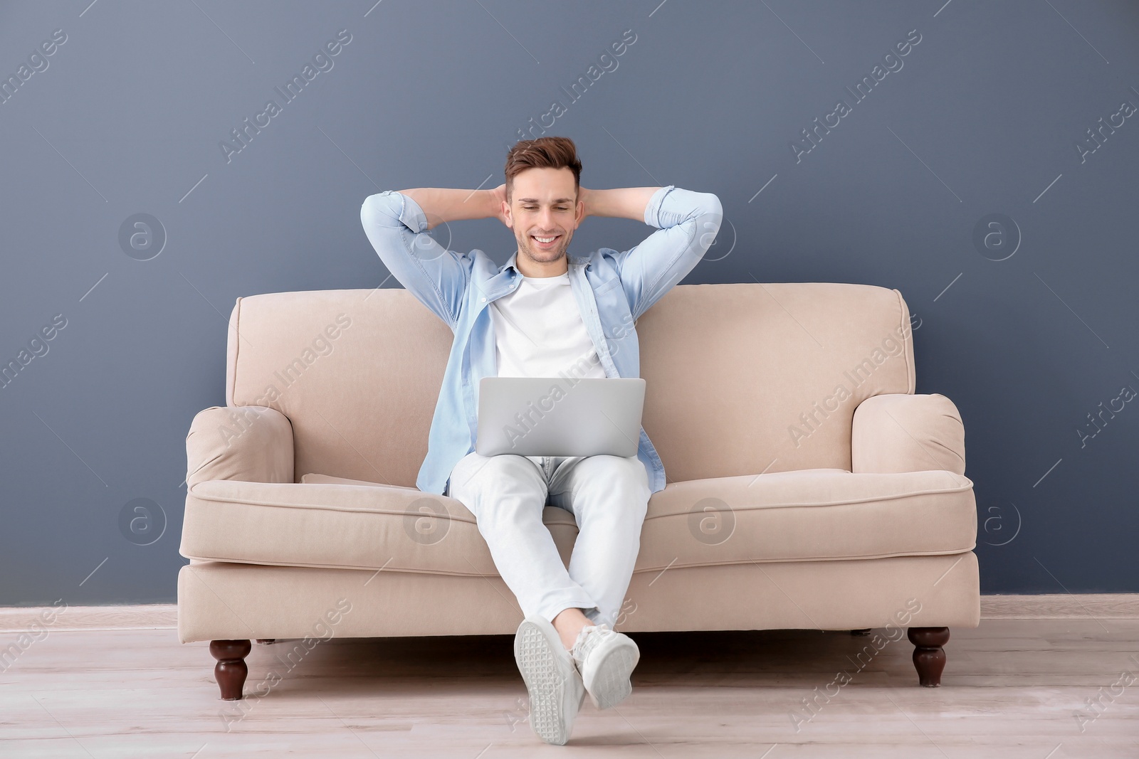 Photo of Handsome young man with laptop sitting on sofa, indoors