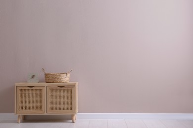 Photo of Wooden cabinet with clock and wicker basket near beige wall, space for text. Interior design