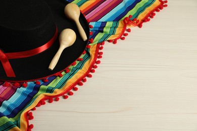 Photo of Black Flamenco hat, poncho and maracas on light wooden table, above view. Space for text
