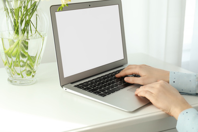 Woman working on modern laptop at white table indoors, closeup