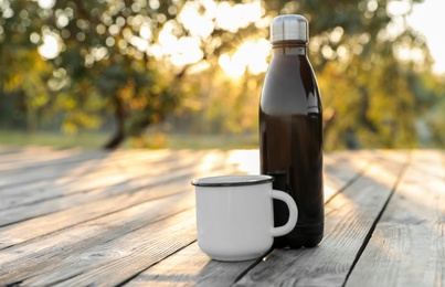 Photo of Modern black thermos bottle and cup on wooden surface outdoors. Space for text