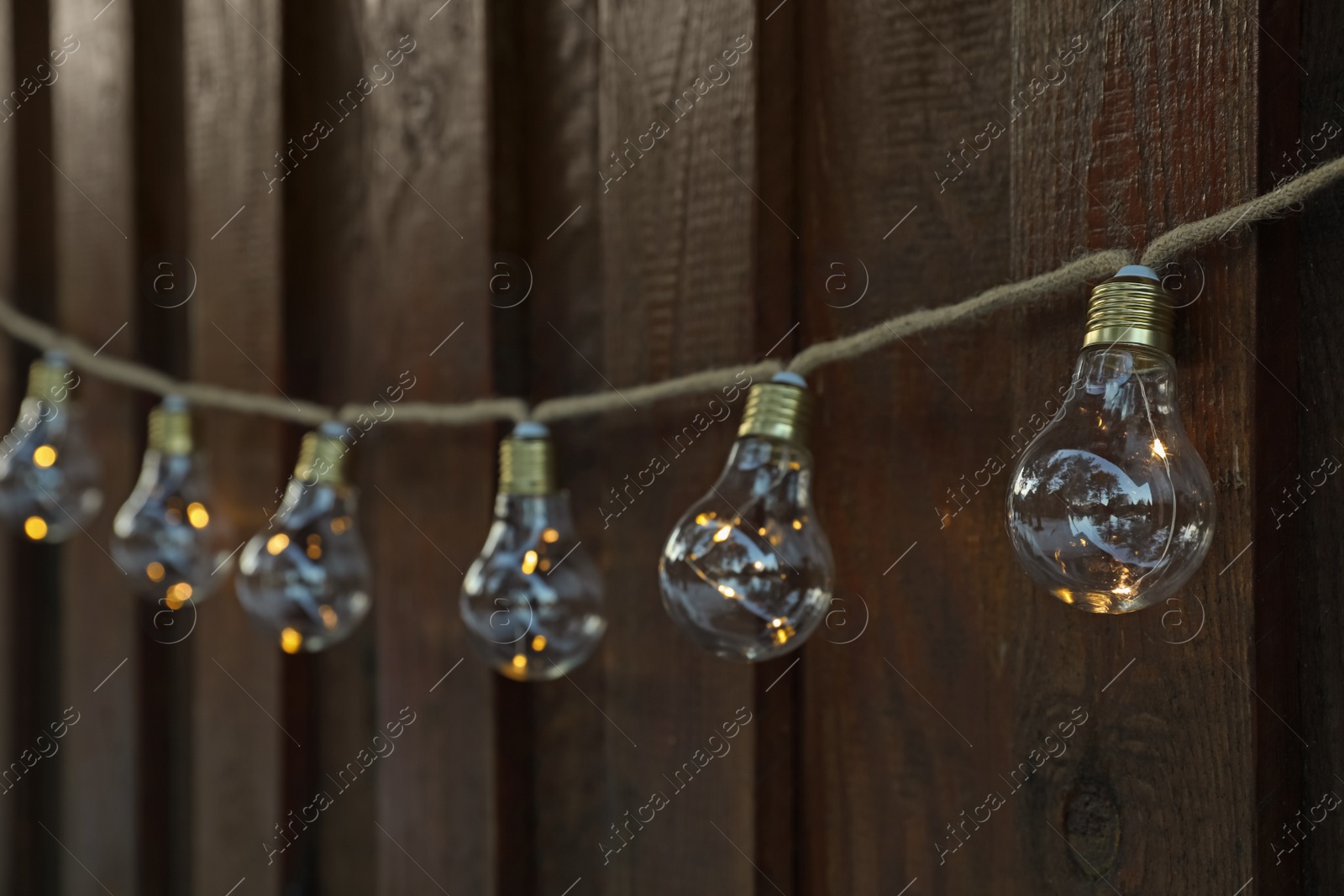 Photo of Garland of lamp bulbs hanging on wooden wall. String lights