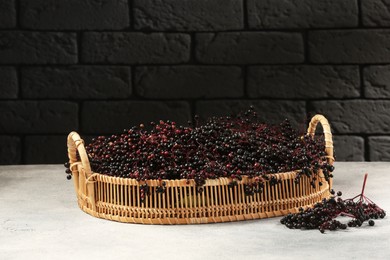 Photo of Wicker basket with ripe elderberries on light grey table near black brick wall