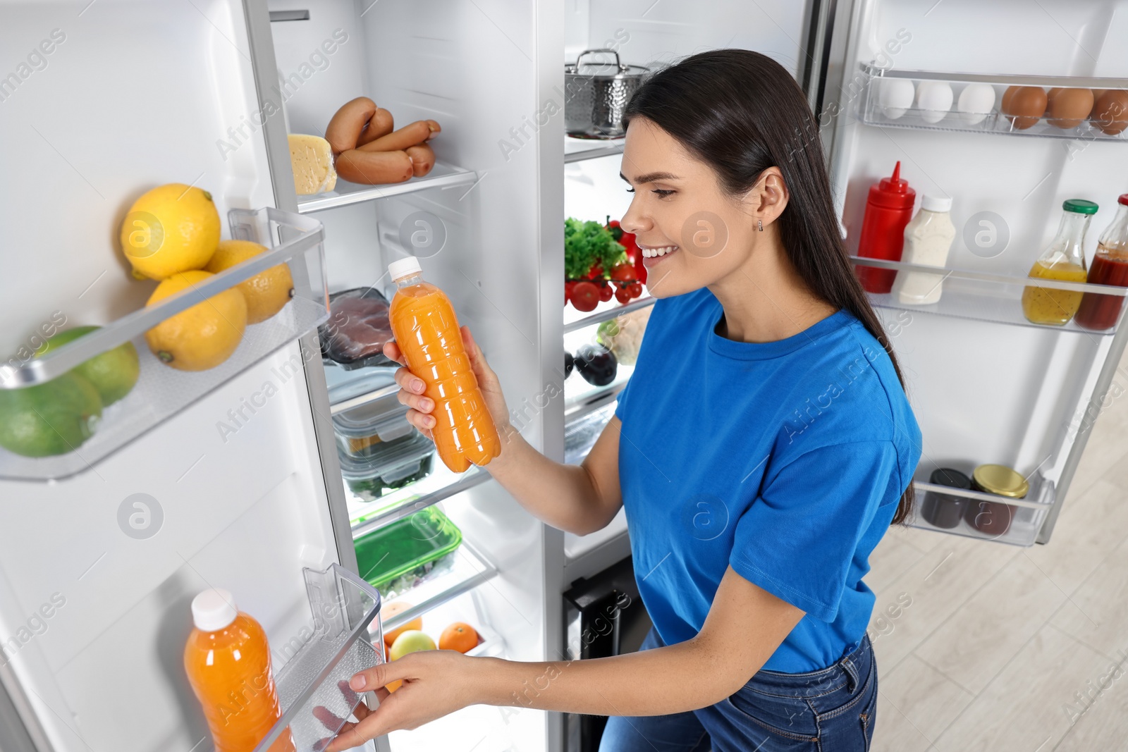 Photo of Young woman taking bottle of juice out of refrigerator indoors, above view