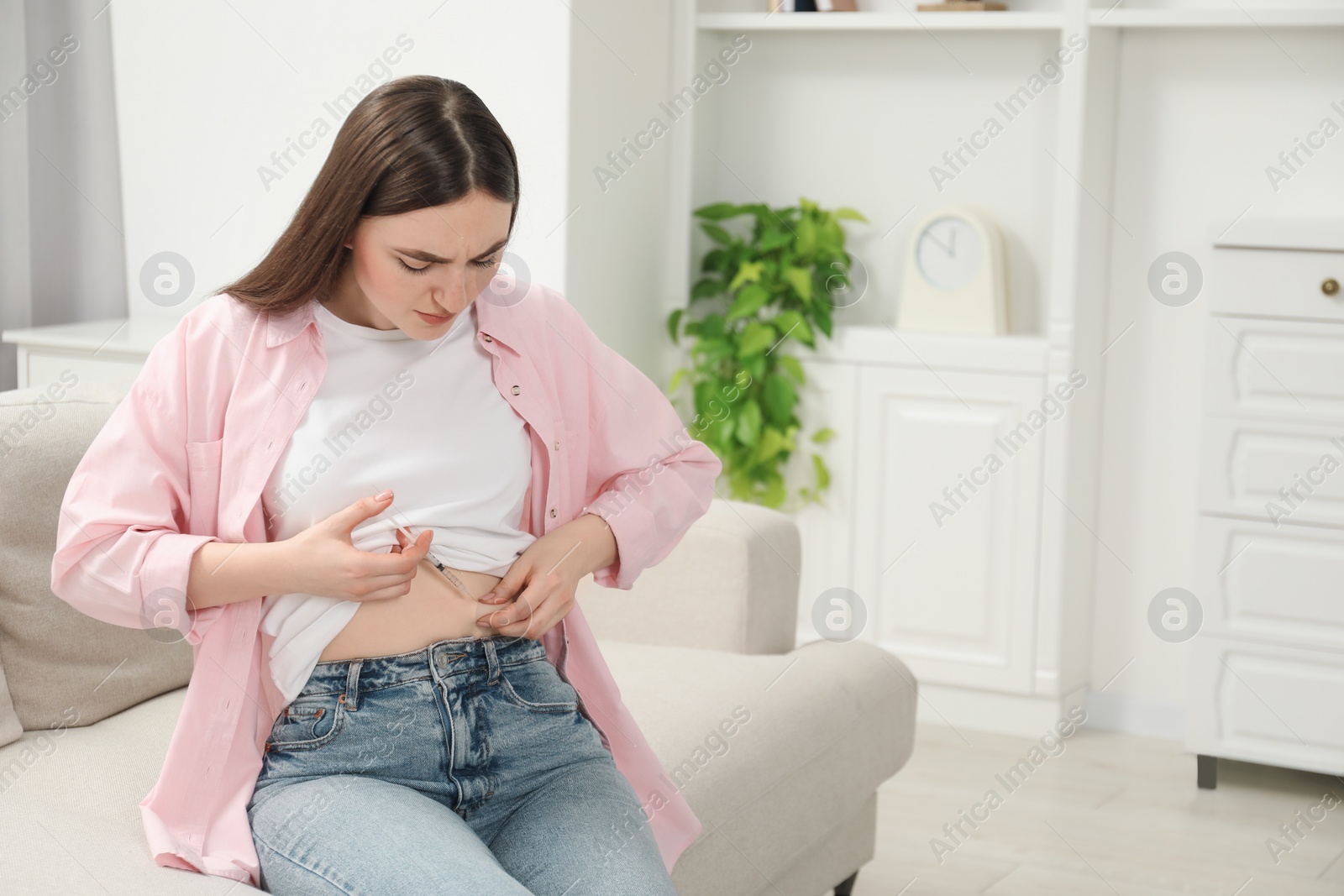 Photo of Diabetes. Woman making insulin injection into her belly on sofa at home, space for text