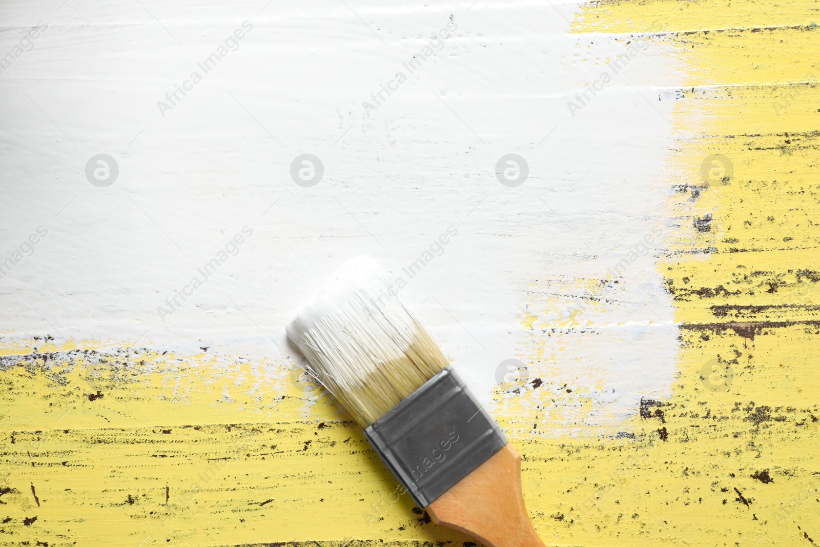 Photo of Paint stroke and brush on yellow wooden table, top view. Space for text