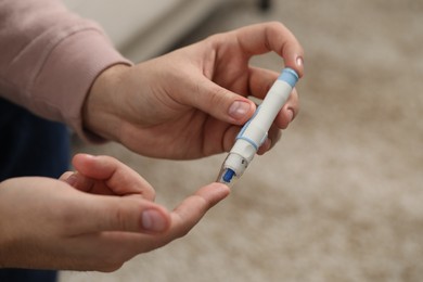 Diabetes test. Man checking blood sugar level with lancet pen on blurred background, closeup. Space for text