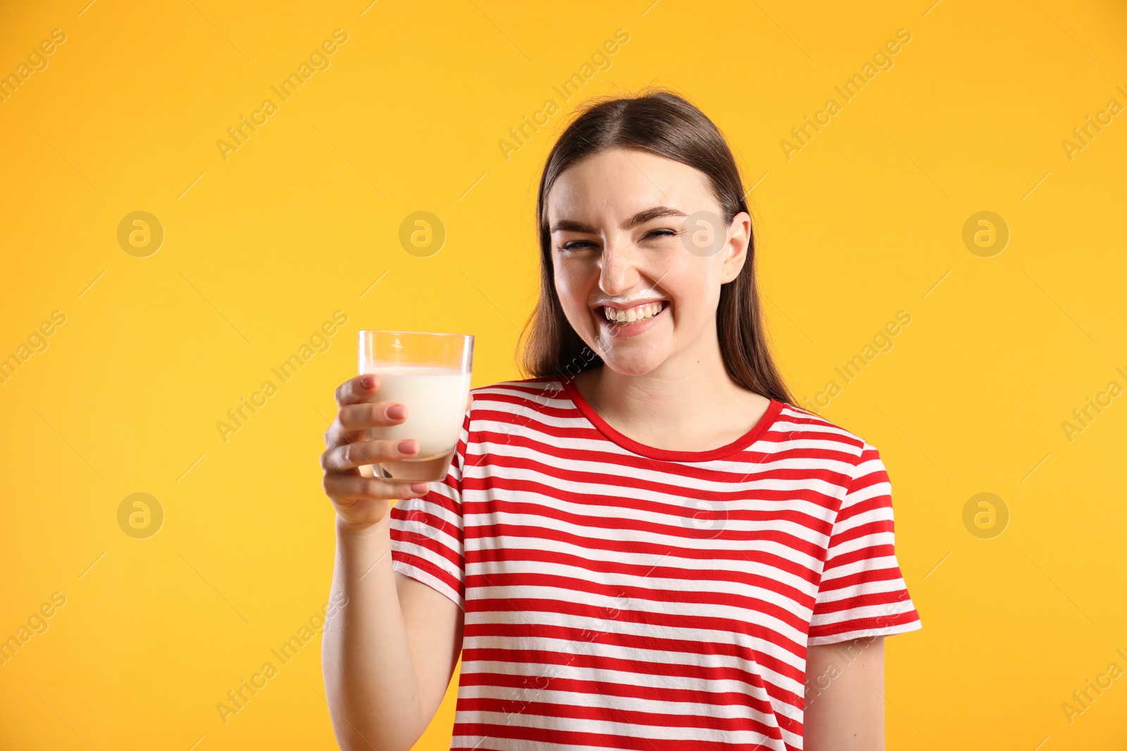 Photo of Happy woman with milk mustache holding glass of tasty dairy drink on orange background