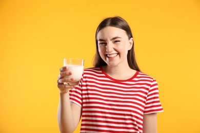 Happy woman with milk mustache holding glass of tasty dairy drink on orange background