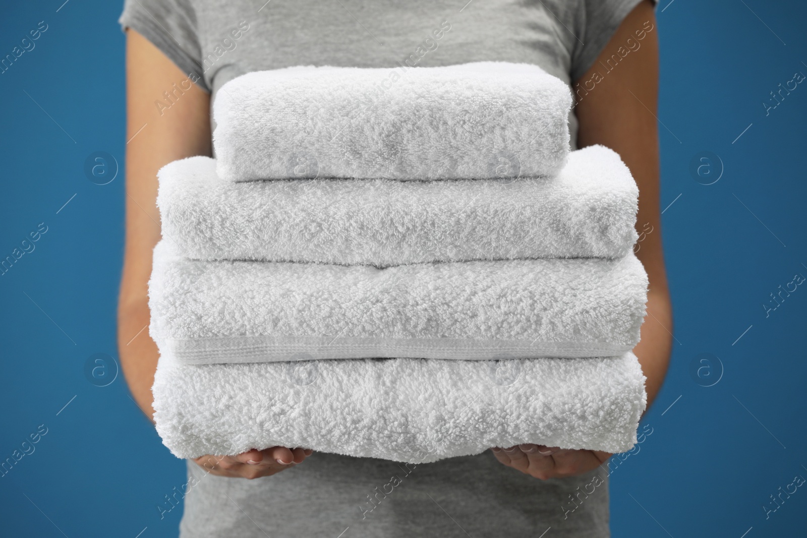 Photo of Woman holding fresh towels on blue background, closeup