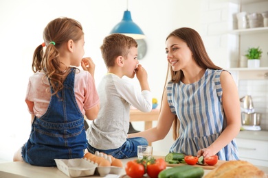 Young woman cooking breakfast for her children in kitchen. Happy family