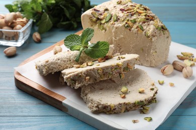 Photo of Pieces of tasty halva with pistachios and mint on light blue wooden table, closeup