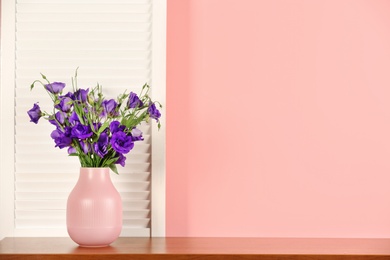 Photo of Beautiful bouquet of purple eustoma flowers in vase near color wall with space for text