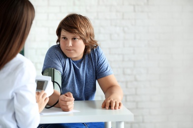 Photo of Female doctor checking overweight boy's blood pressure in clinic