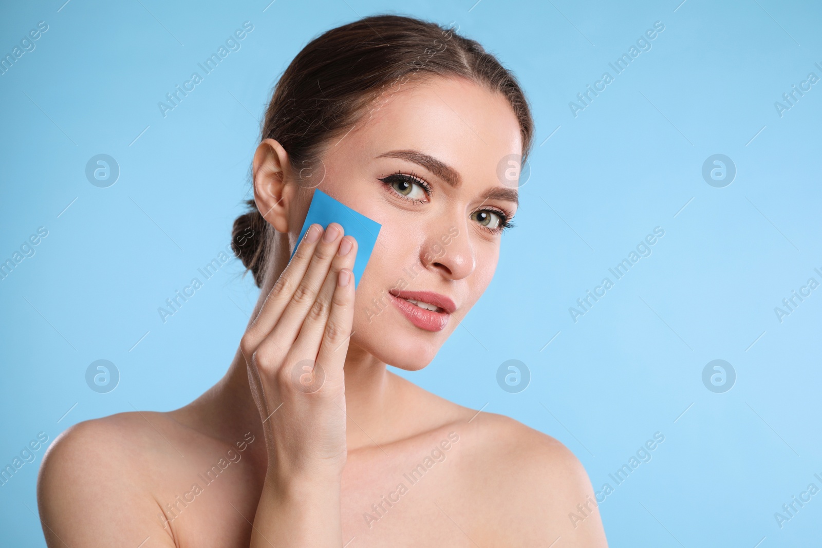 Photo of Beautiful woman using mattifying wipe on light blue background