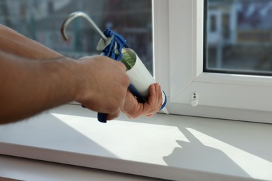Man sealing window with caulk indoors, closeup