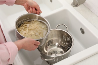 Photo of Woman draining pasta into colander at sink, closeup