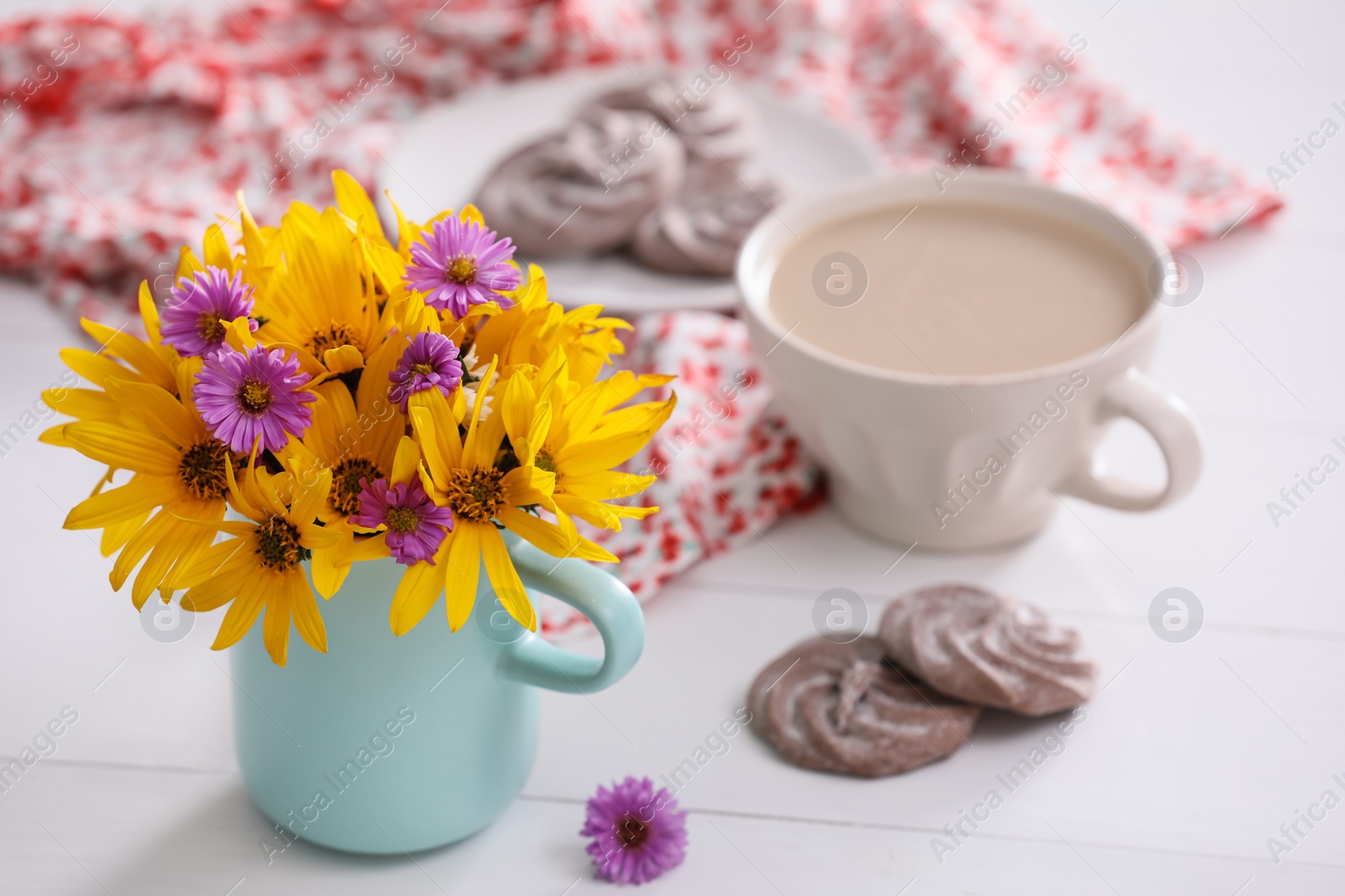 Photo of Beautiful bright flowers, cup of coffee, cookies and fabric on white table. Space for text