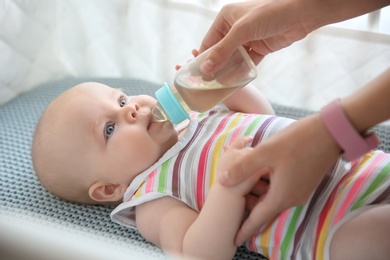 Lovely mother giving her baby drink from bottle in cot