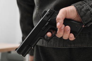Man hiding gun behind his back indoors, closeup. Armed robbery