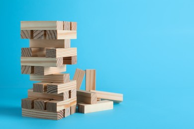 Photo of Jenga tower made of wooden blocks on light blue background, space for text