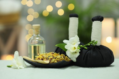 Photo of Spa composition. Herbal massage bags, essential oil and dry flowers on towel against blurred lights