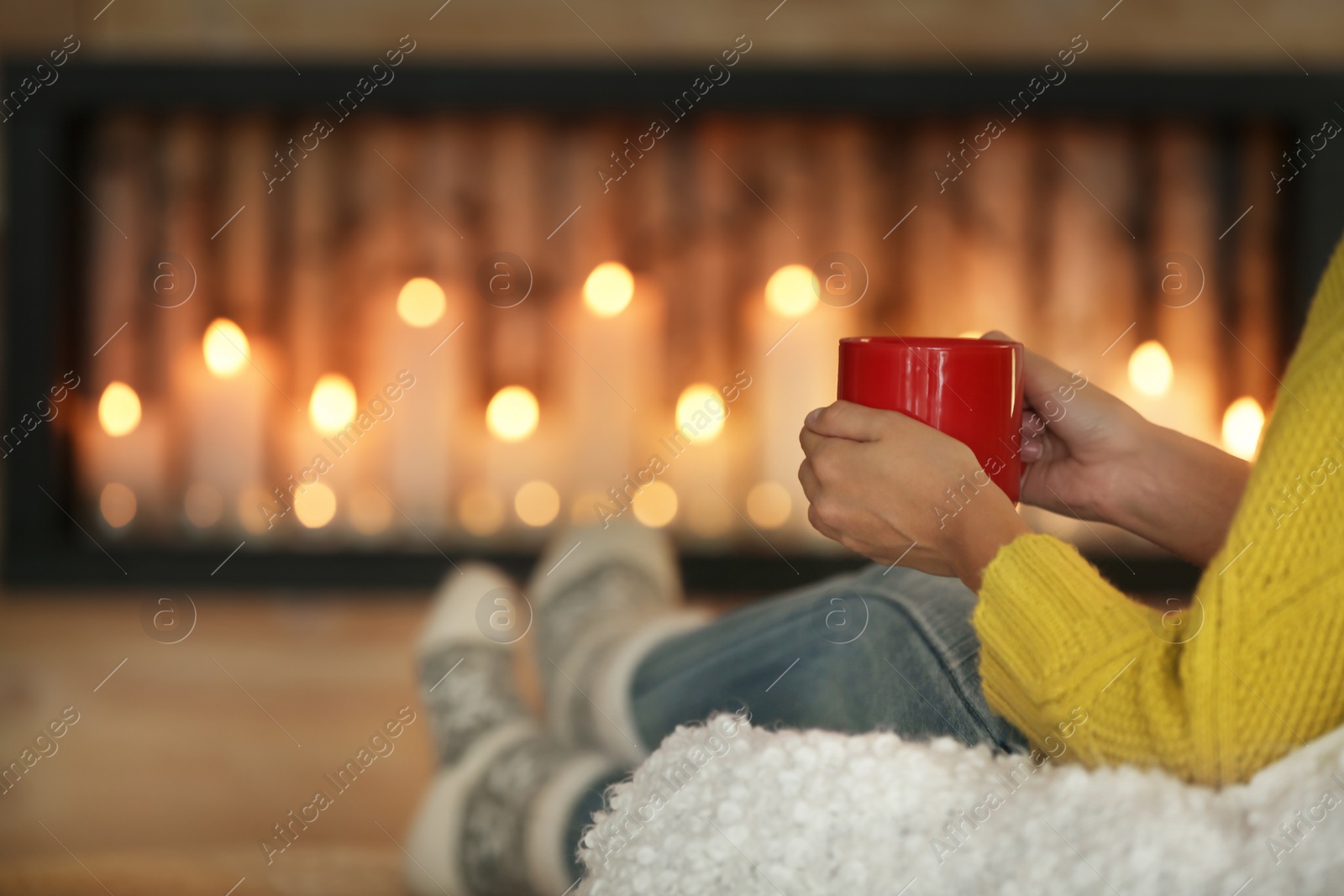 Photo of Woman with cup of hot drink near decorative fireplace indoors, closeup. Winter atmosphere