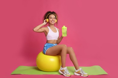 Beautiful African American woman with headphones  on yoga mat against pink background