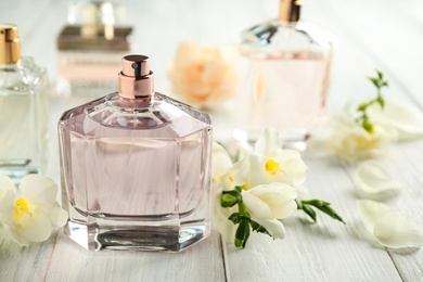 Photo of Bottles of perfume and beautiful flowers on white wooden table. Space for text