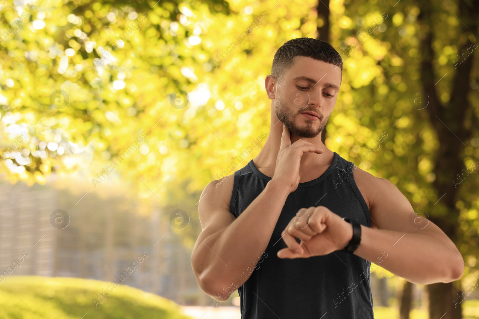 Photo of Attractive serious man checking pulse after training in park on sunny day. Space for text