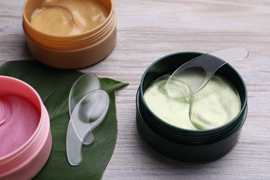 Photo of Packages of different under eye patches and tropical leaf on wooden table. Cosmetic product
